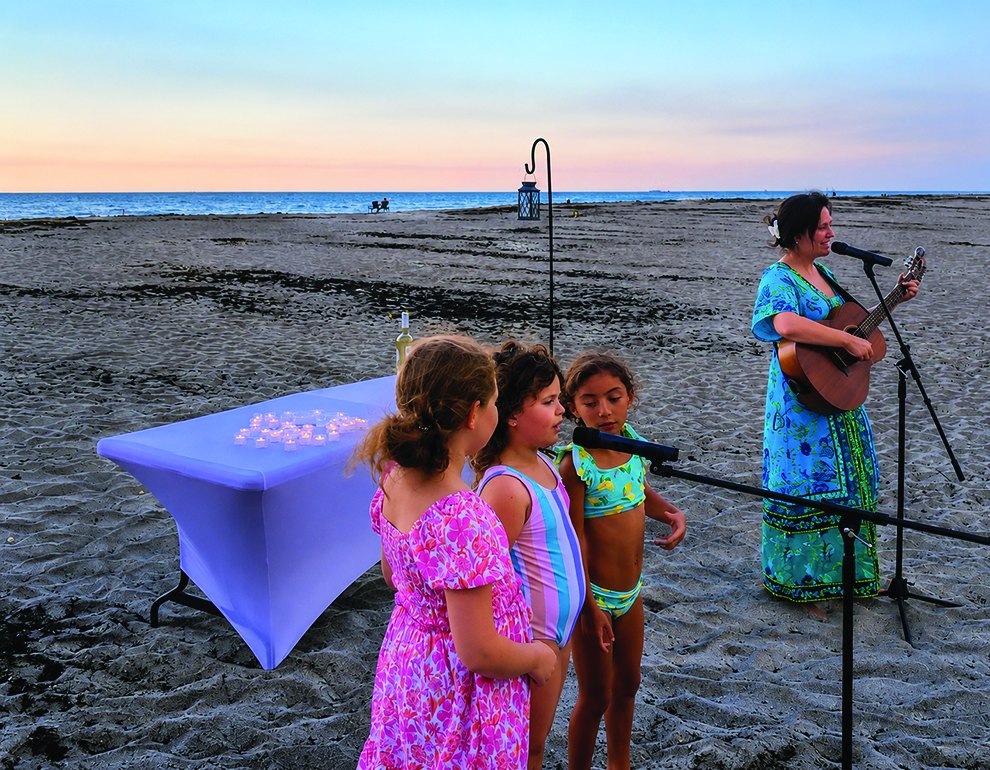 Children gather as Cantor Abbie Strauss leads Beach Shabbat with guitar at sunset