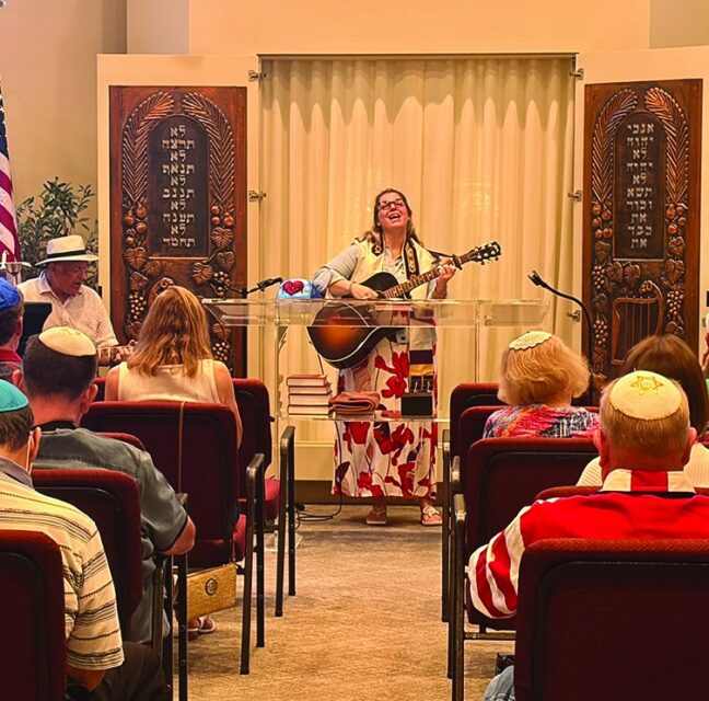 Rabbi Cantor Danielle Bensimhon playing guitar at the Red, White and Blue Shabbat service