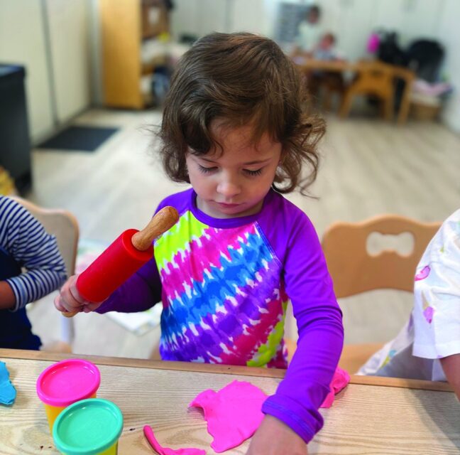 Young camper shaping pink play dough at a Camp Catan craft table