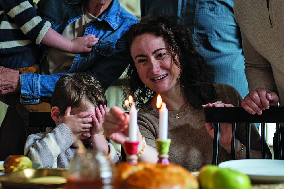 Mother lights Shabbat candles while her young son covers his eyes