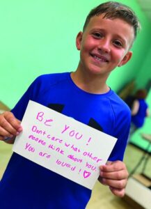 Boy holding a handmade sign reading Be You at a Kohl JVC project